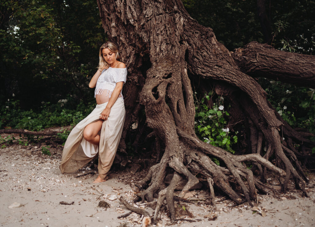 Schwangere lehnt beim Babybauchshooting an einem Baum an